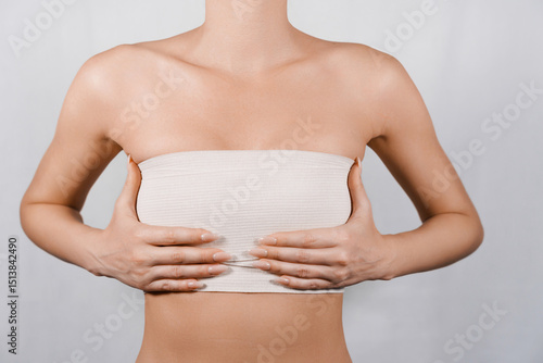 Patient Post-Breast Reduction: Woman Holding Bandaged Breasts While Recovering in Medical Setting.