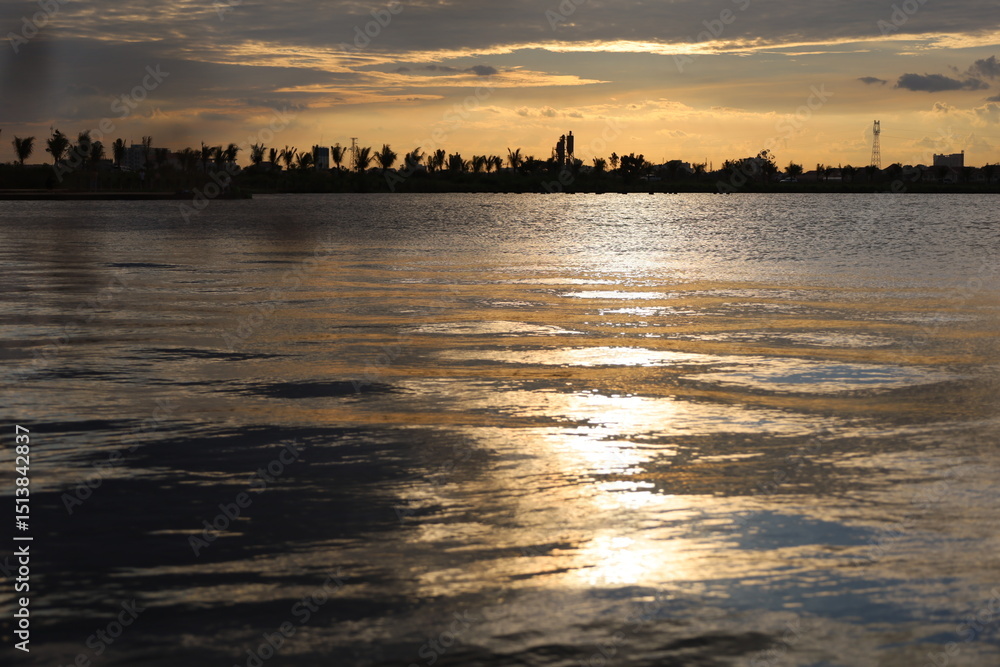 Naklejka premium Golden sunlight reflects on tranquil river water under an expansive sky
