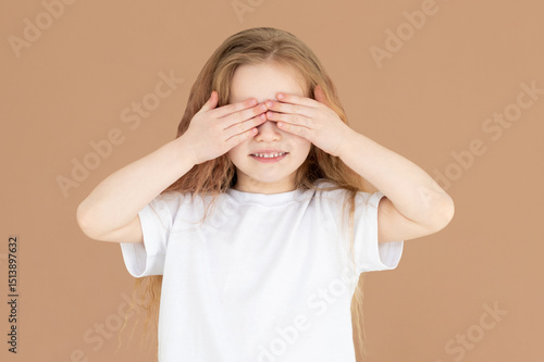 Shy child who is ashamed of his bad behavior without showing his tears. a little girl covering her eyes playing hide-and-seek on a brown background. Body language