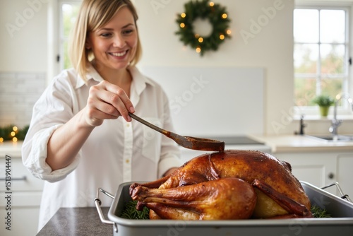 A white woman is basting a roast duck with sauce in a large oven tray in a bright kitchen decorated for the holidays. The background shows a wreath and fairy lights