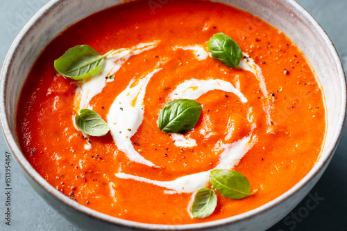 Tomato soup with cream in a white bowl on grey background. Close up.