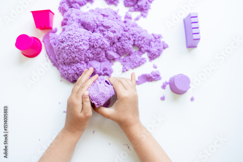 Child hands playing with purple kinetic sand on white surface