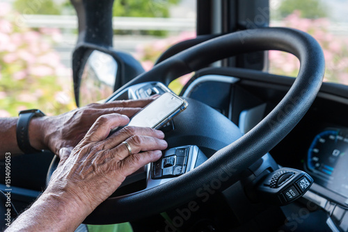 The hands of a senior truck driver texting on his mobile phone while resting on the steering wheel, highlighting the hardships of life on the road away from family.