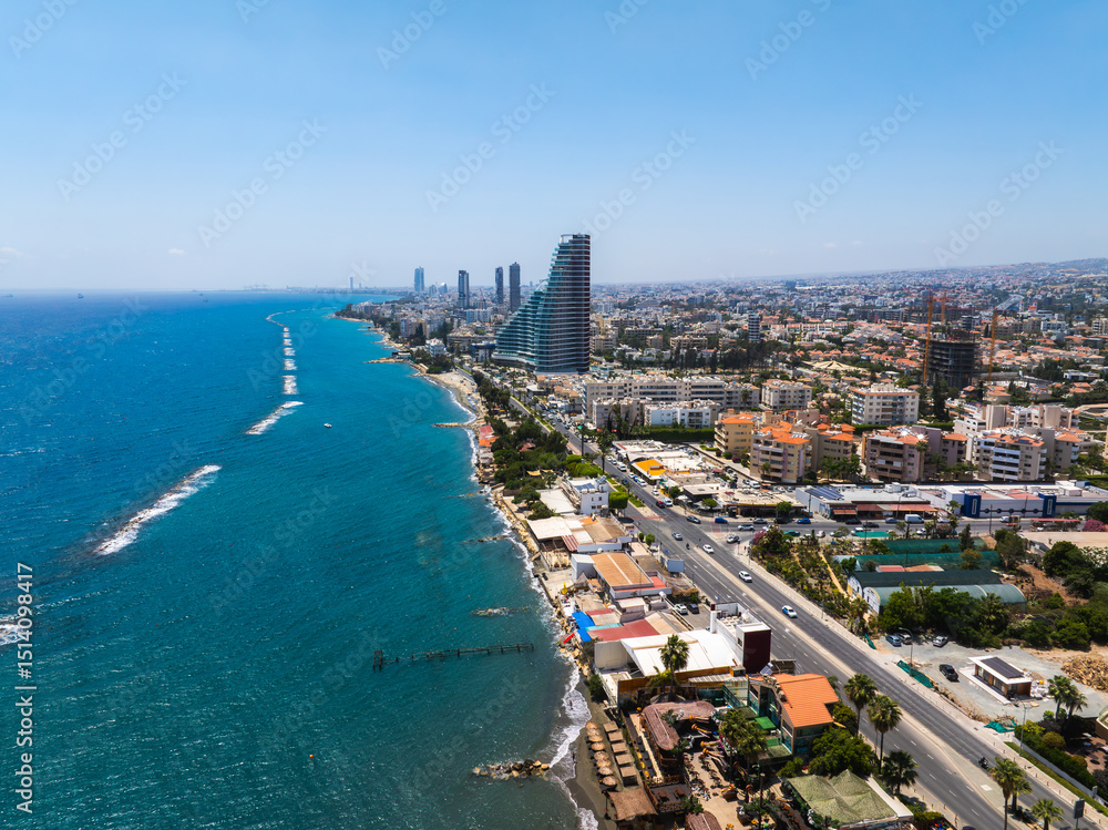 Fototapeta premium Aerial view of Limassol, Cyprus, featuring modern high rises, a curved tower, sandy beaches, rocky shores, palm lined roads, and the Mediterranean Sea.