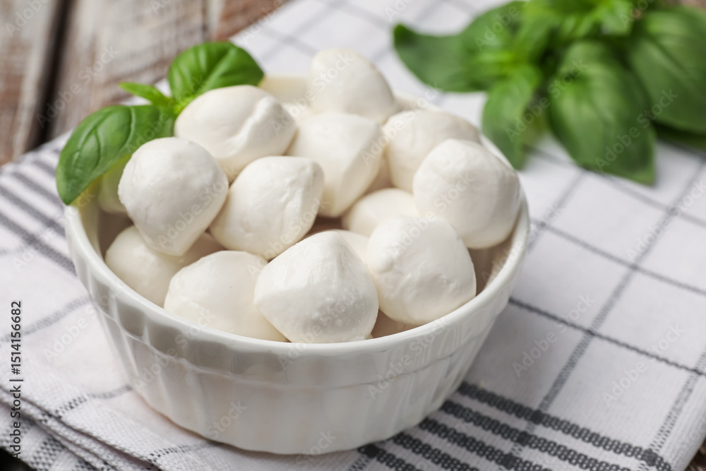 Tasty mozzarella cheese balls in bowl and basil on table, closeup Tasty mozzarella cheese balls in bowl and basil on table, closeup