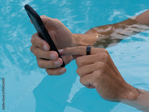 Hands in pool water wearing black smart ring health tracker and using smartphone app.