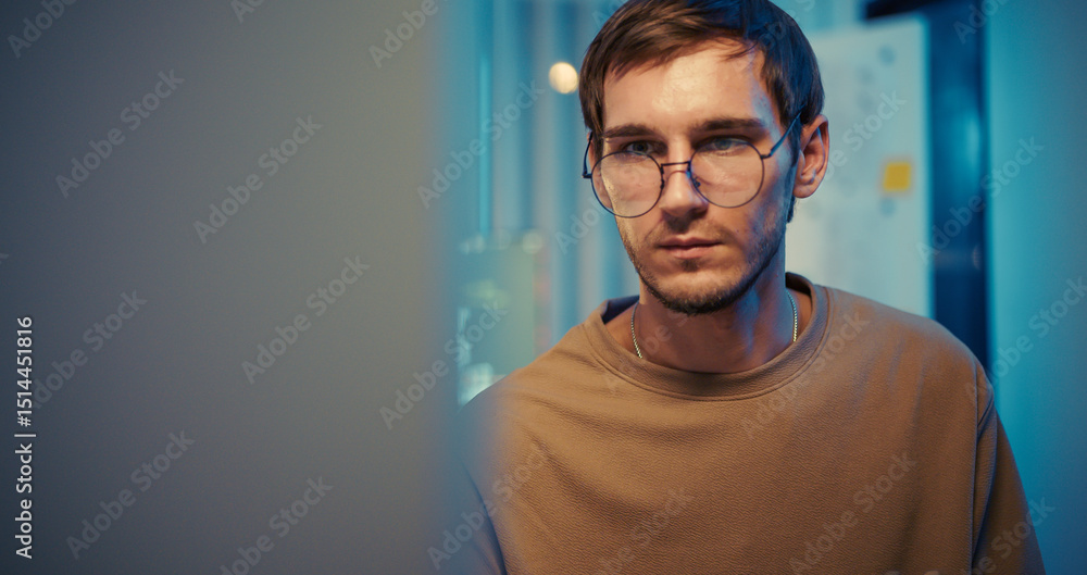 Fototapeta premium Caucasian male engineer looks at computer screen in modern tech office at night. Deep concentration during software analysis and programming task.