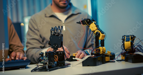 Close-up of engineers working on robotic arms in a modern tech workspace. Focus on hardware development, coding, and robotics prototyping.
