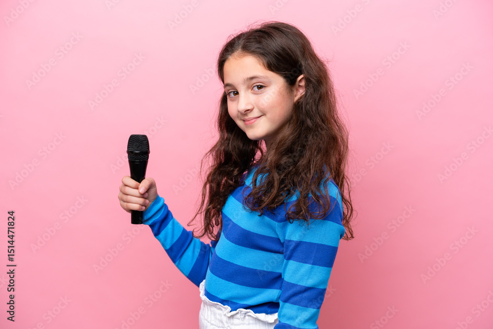 Little singer girl picking up a microphone isolated on pink background smiling a lot Little singer girl picking up a microphone isolated on pink background smiling a lot