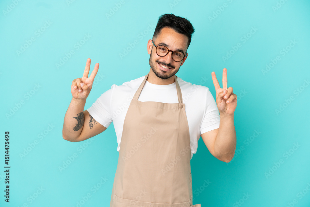 Fototapeta premium Restaurant waiter caucasian man isolated on blue background showing victory sign with both hands