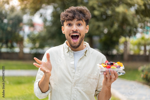 Young Arabian handsome man holding a bowl of fruit at outdoors with shocked facial expression
