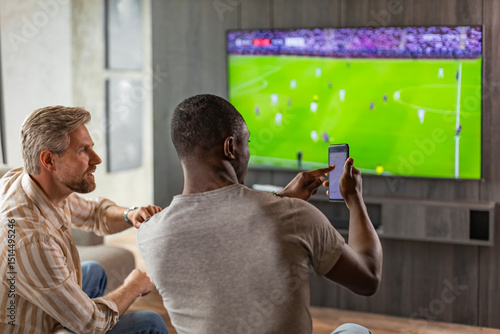 Foto Two friends holding smartphone with sports bets app while watching football matc