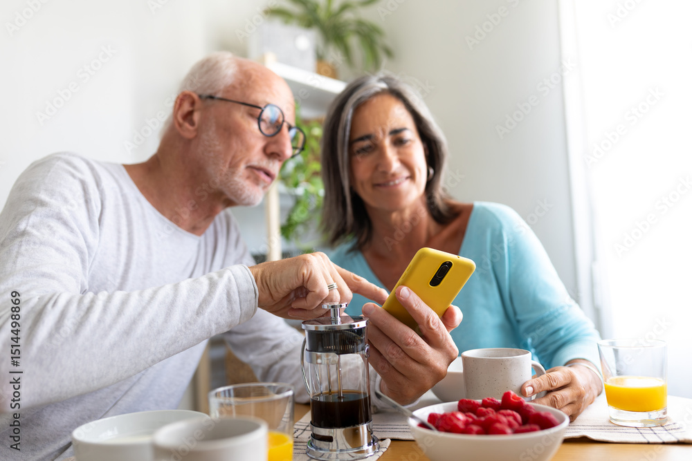 Happy mature couple having healthy meal at home looking at mobile phone. Selective focus on phone. Happy mature couple having healthy meal at home looking at mobile phone. Selective focus on phone.