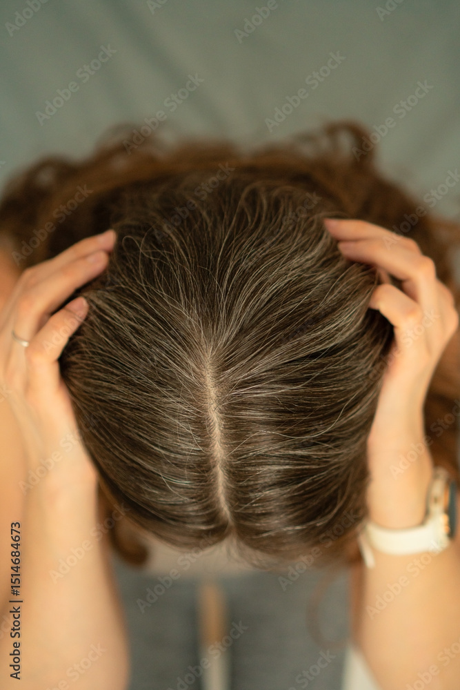 Naklejka premium Close-up view from above of a woman touching her scalp and showing gray roots. Beauty in aging, self-acceptance, and gentle hair care. Natural transformation, soft light, healthy texture.