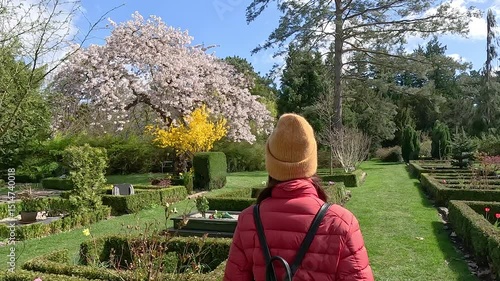A woman walks through a cemetery during the day against the backdrop of flowering trees.