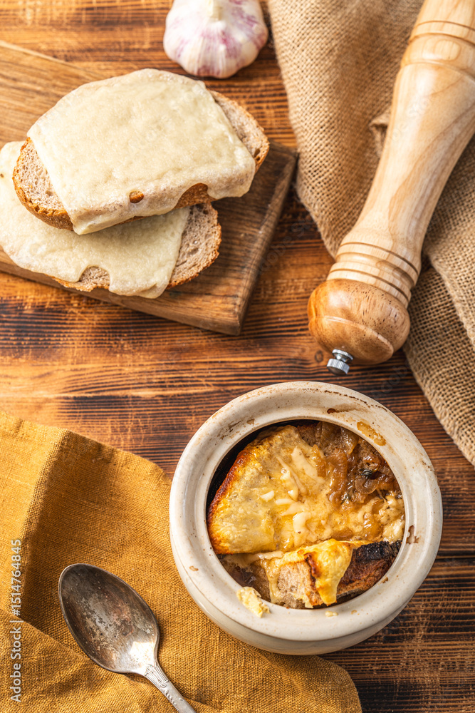 Fototapeta premium Onion soup in a pot according to a traditional French recipe with a cheese crust, on a wooden background with toasted bread and cheese.