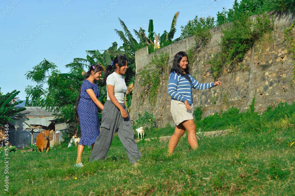 Fototapeta premium Full of joy, the girls cross the field while cows and goats graze around them.
