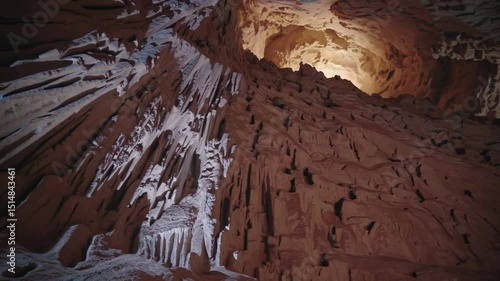 Majestic cave interior with jagged red rock formations and glowing light from ceiling opening

