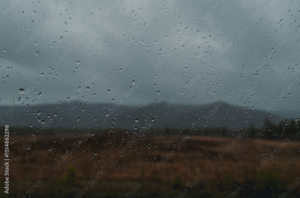 Raindrops gather on the glass, obscuring the view of tranquil hills in the distance under a gray sky. Raindrops gather on the glass, obscuring the view of tranquil hills in the distance under a gray sky.