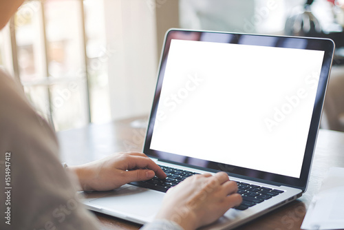 A close-up of a person's hands typing on a laptop with a blank screen, in a cafe setting.