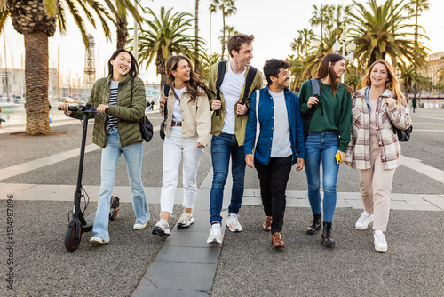 Photography Group of students walking and talking along barcelona's seafront, one of them using electric scooter