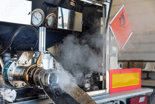Open discharge outlet of a tanker truck carrying hazardous materials during the cleaning process at a wash station, releasing vapor and product residues.