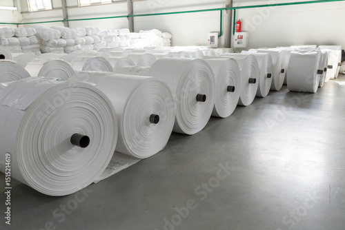 Large white rolls of polypropylene are laid out in rows in the warehouse of the factory.