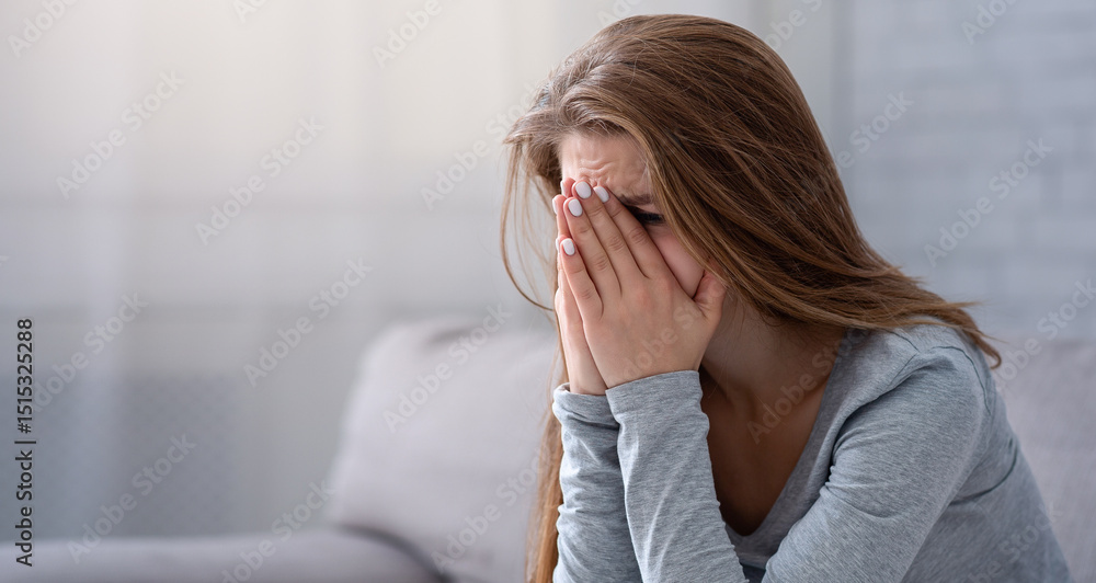Εκτύπωση καμβά Young woman burying her face in hands and crying, feeling depressed or desperate on sofa indoors