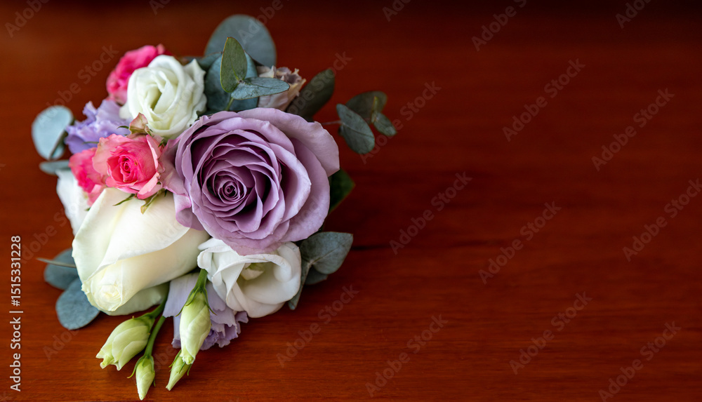 Obraz premium Boutonniere with lavender and white roses on wooden surface. A small floral boutonniere featuring lavender, white, and pink roses. Space for text.