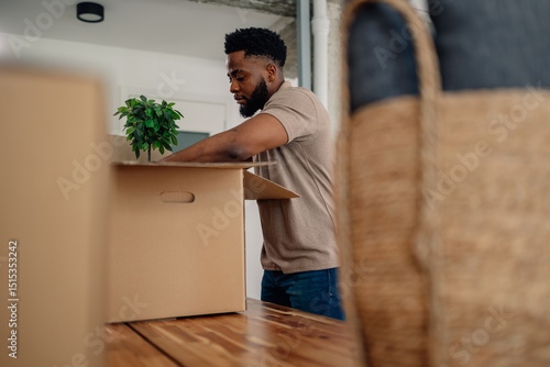 Bild auf Leinwand Man unpacking cardboard box with plant in new home