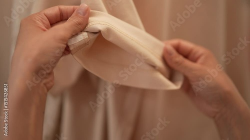 Skilled seamstress examining beige sleeve seam, focusing on precise stitching and quality control during professional garment manufacturing process. Tailor inspecting seam on sleeve of garment closeup