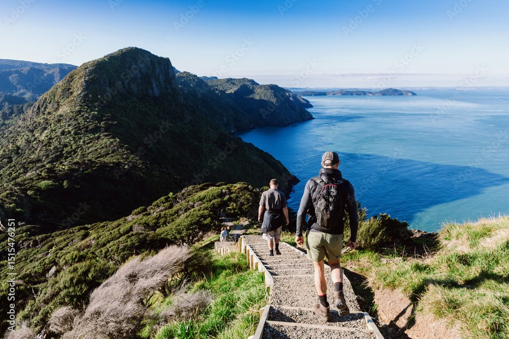 Ταπετσαρία Hikers descend wooden steps on a trail overlooking the ocean in Whatipu, Auckland, New Zealand