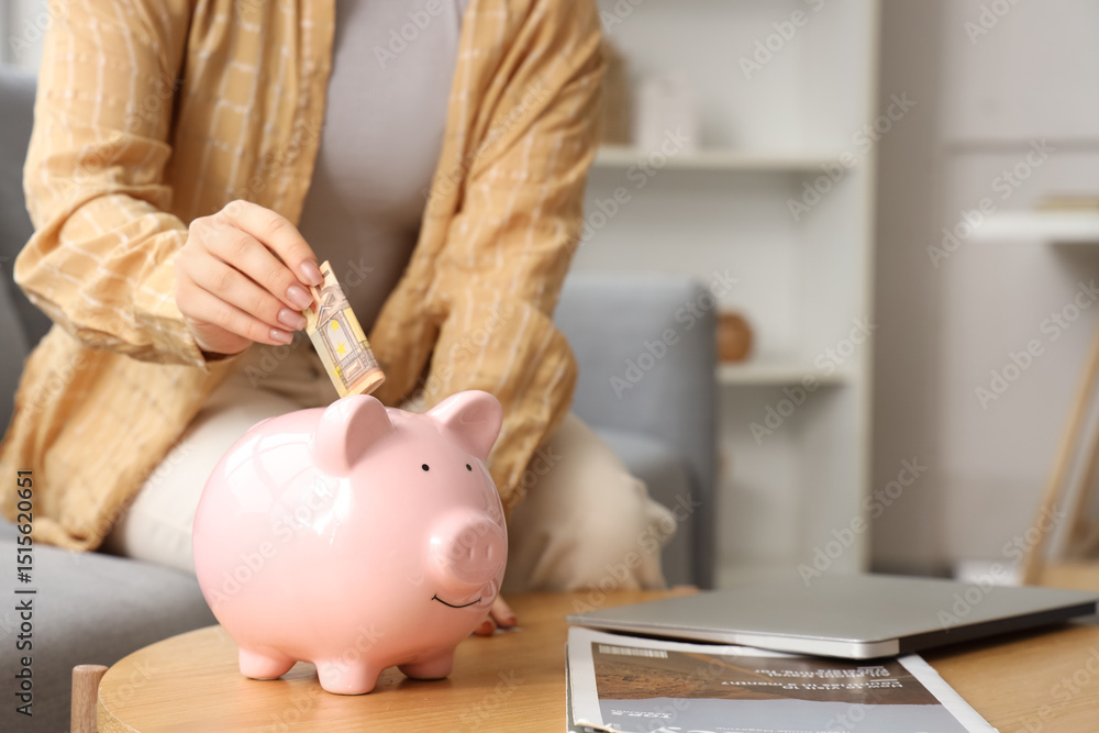 Φωτογραφία Young woman putting euro banknote into piggy bank on table at home, closeup