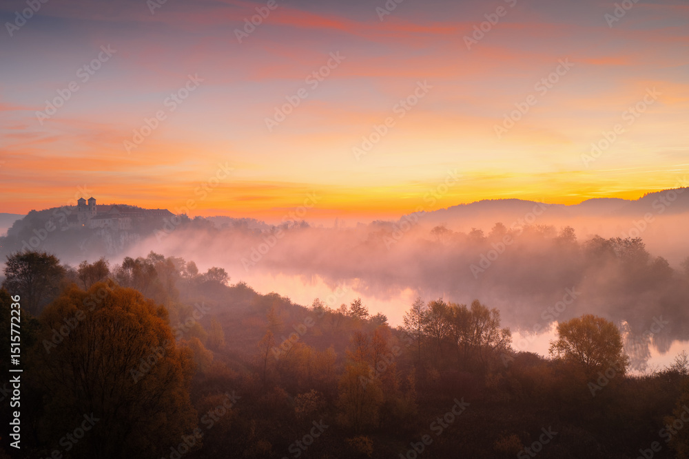 Obraz premium Picturesque orange sunrise over the river with morning mists. View of the Benedictine Abbey in Tyniec. Autumn landscapes of Poland.