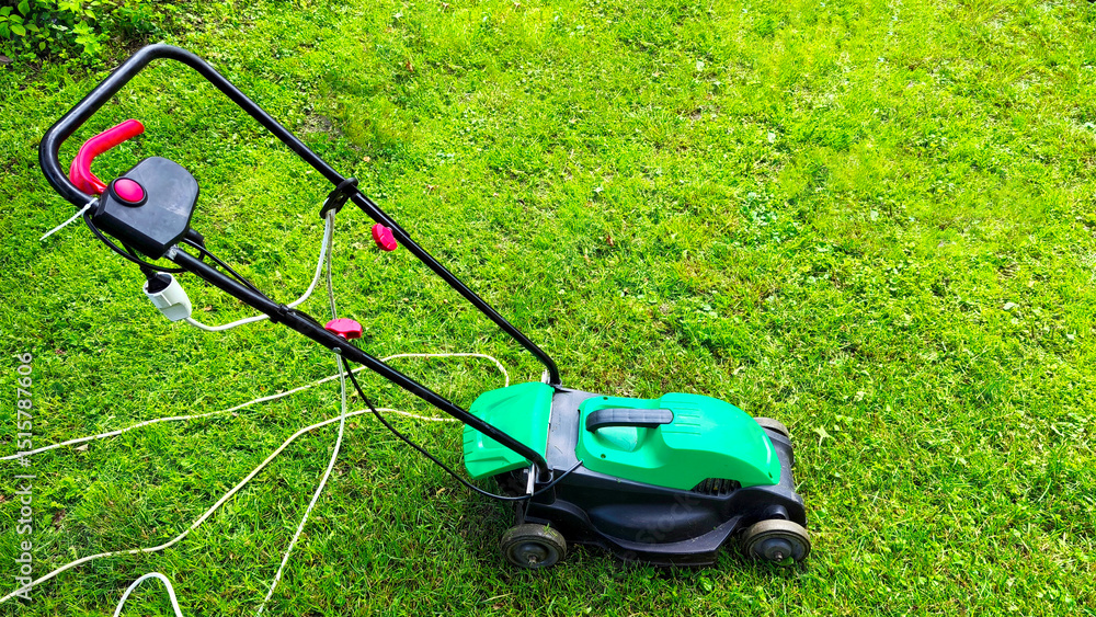 Fototapeta premium Modern green lawn mower cutting bright juicy green grass. Garden tools. Lawn mower on the lawn. Professional lawn maintenance