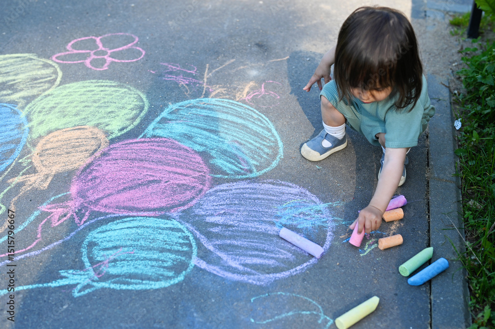 Naklejka premium Toddler girl drawing by chalks on playground on summer day