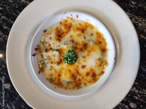 Baked spinach with creamy cheese topping, golden and bubbly, served hot in a white dish on a marble table.