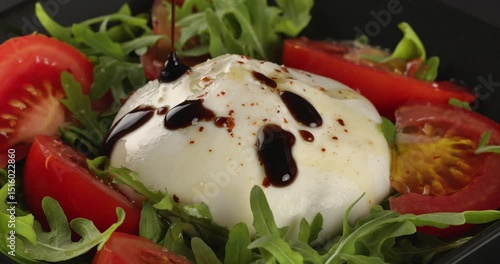 Burrata cheese with tomatoes and arugula drizzled with balsamic vinegar. Close-up footage on the rotating table.