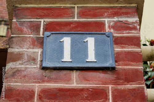 Numéro 11. Plaque de numéro de rue sur façade de brique rouge.