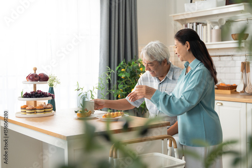 Foto Elderly Asian woman lovingly looks at her husband while he eats breakfast at home