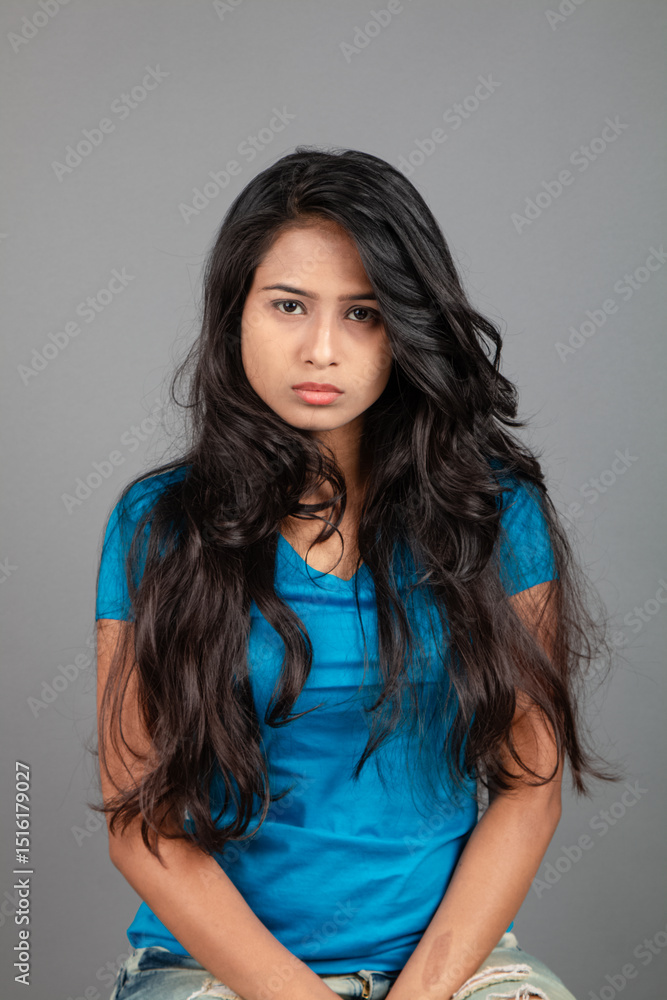 Fototapeta premium A young woman confidently poses wearing blue t-shirt, distressed denim jeans, heels, showcasing a casual urban style with charm and elegance, suitable for haircare, freedom, self-expression project