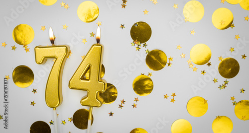 Photography Number 74 golden celebration birthday candle on white with confetti background
