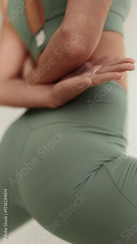 Vertical closeup of a woman in green activewear clasping hands behind her back, highlighting a fitness stretch routine.