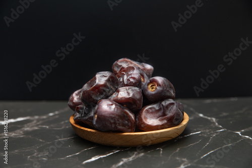 Dates fruit in wooden dish isolated on dark background.