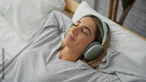 Woman relaxing on bed wearing headphones in a cozy bedroom setting, exuding comfort and tranquility with closed eyes, enjoying a peaceful moment at home.