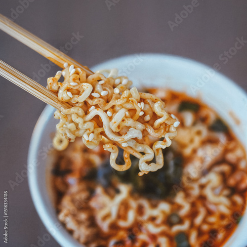 Close-up of cooked instant noodles held with chopsticks over a bowl of ramen