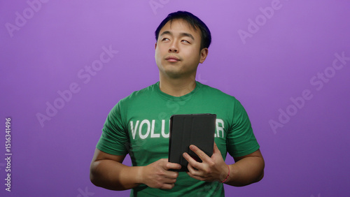 Fotografía Young man in green volunteer shirt holds tablet against purple background, showcasing an isolated setting emphasizing community involvement and digital engagement