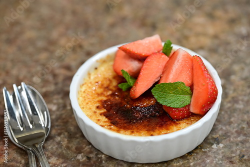Obraz na plátně Close-up of traditional crème brûlée dessert with strawberries – caramelized sugar crust and creamy custard in shallow dish