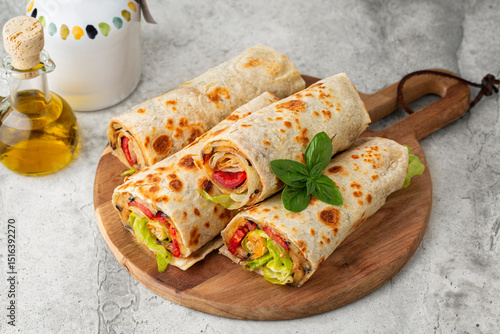 Piadina or tortilla on a wooden board. Wraps made with a soft flatbread rolled around a filling with vegetables and cheese, fried eggplant, tomato, lettuce. Vegetarian food concept.