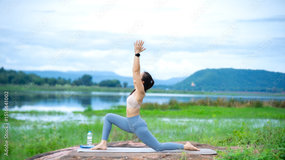 A woman is doing yoga on a rock by a lake. She is wearing a white tank top and blue pants A woman is doing yoga on a rock by a lake. She is wearing a white tank top and blue pants